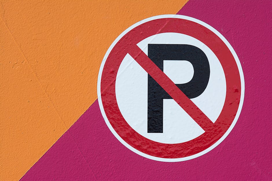 Close-up of a round, red-bordered 'No Parking' sign with a bold black 'P' crossed out in red, mounted on a vibrant wall painted with large patches of orange, pink, and purple. The sign is positioned o