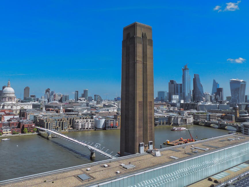 A high-angle view of the London skyline featuring The Leadenhall Building, also known as the Cheesegrater, with a clear blue sky in the background. The River Thames is visible at the bottom of the ima